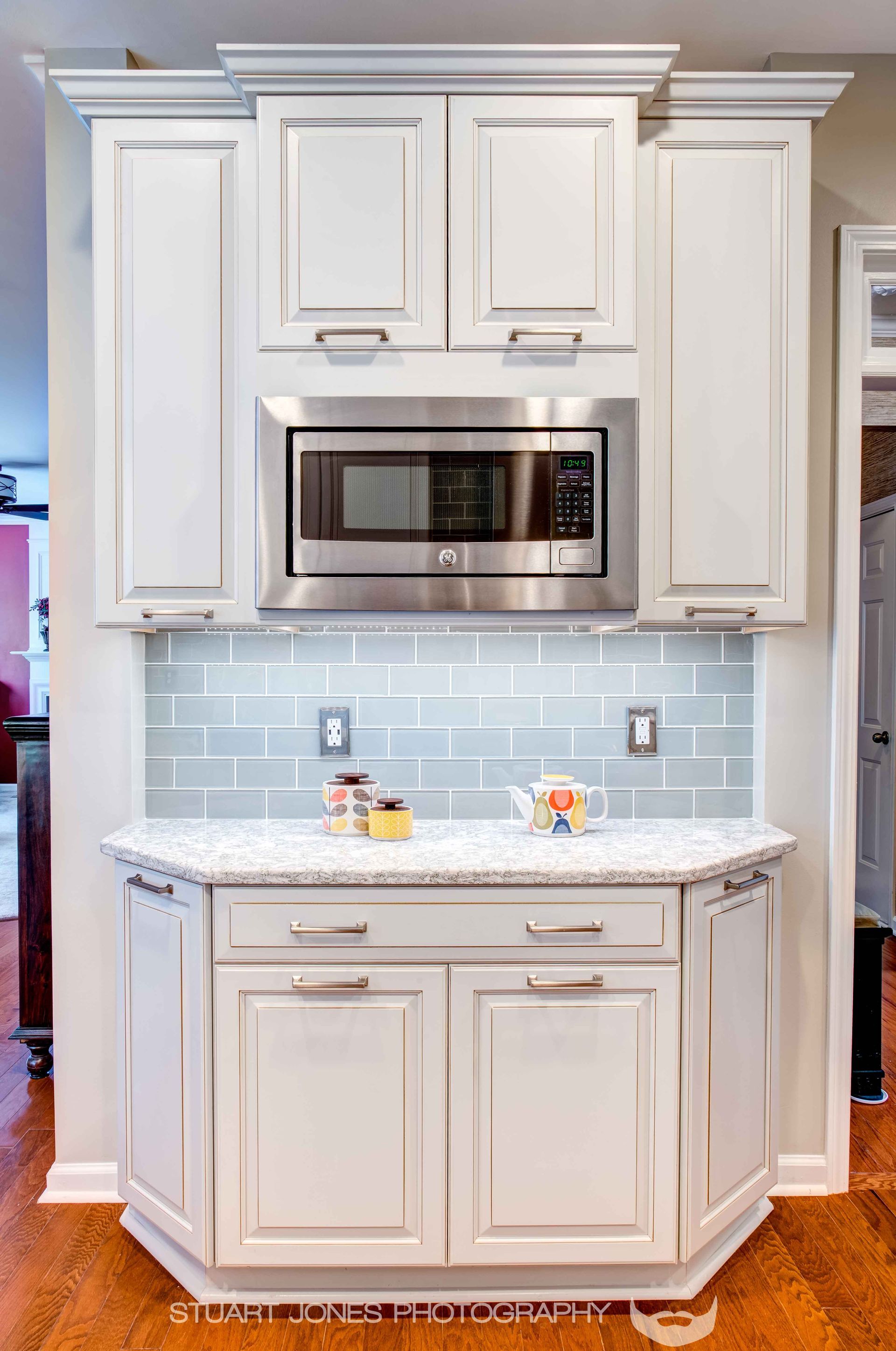 White kitchen cabinet with built-in stainless steel microwave and light blue tile backsplash