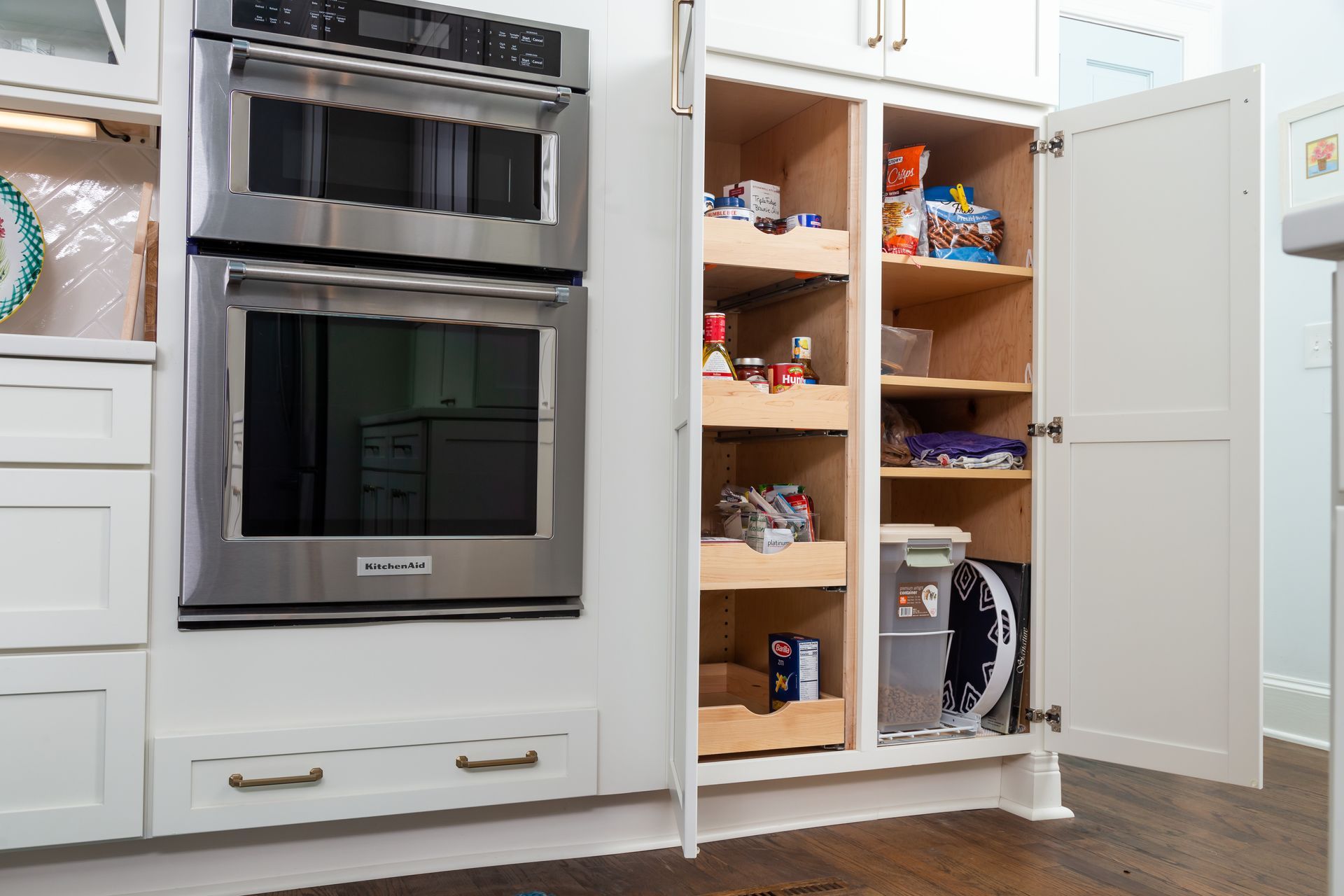 Kitchen with built-in stainless steel oven and open pantry cabinets showing stored groceries.