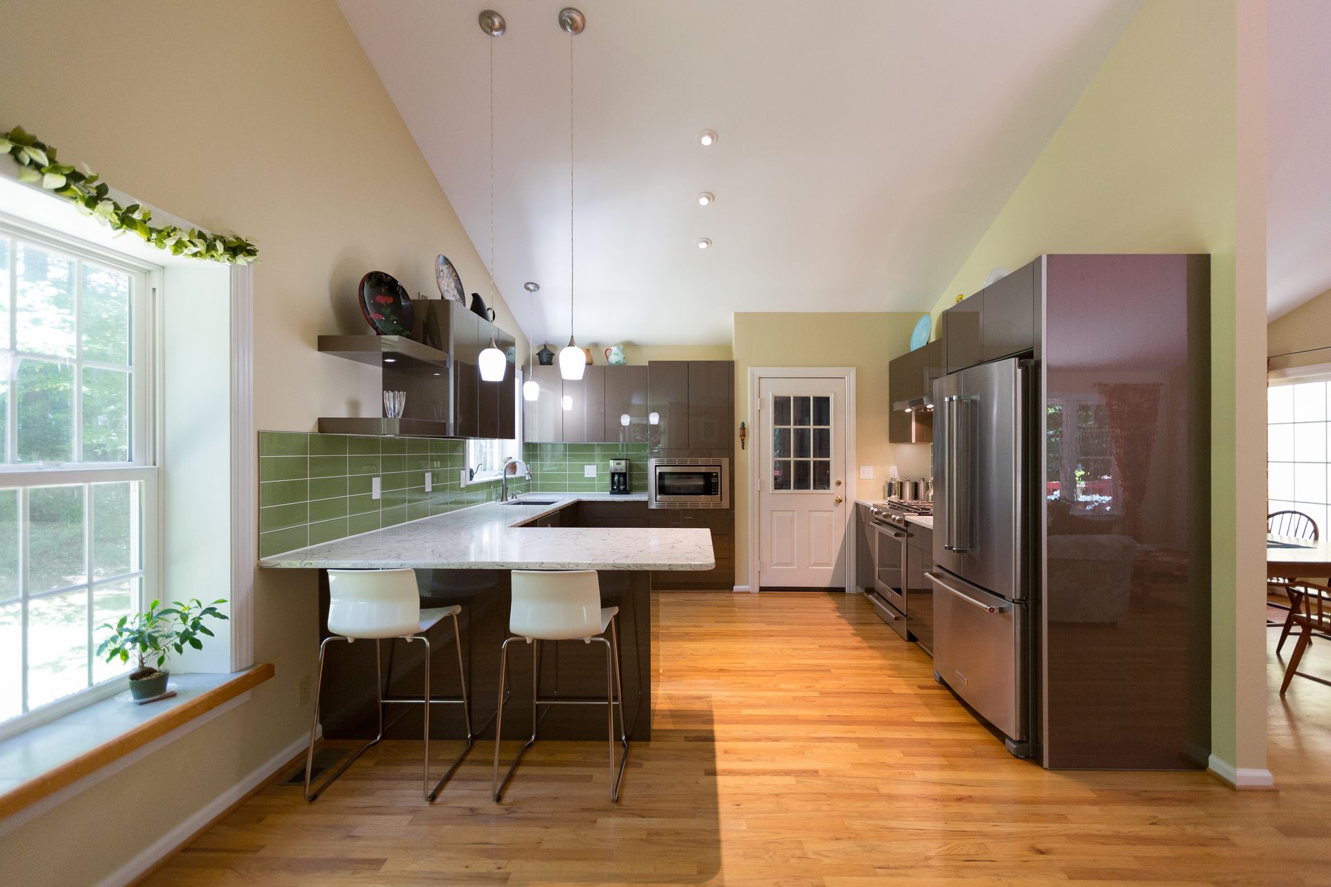 Modern kitchen with green backsplash, island seating, hardwood floors, and large windows