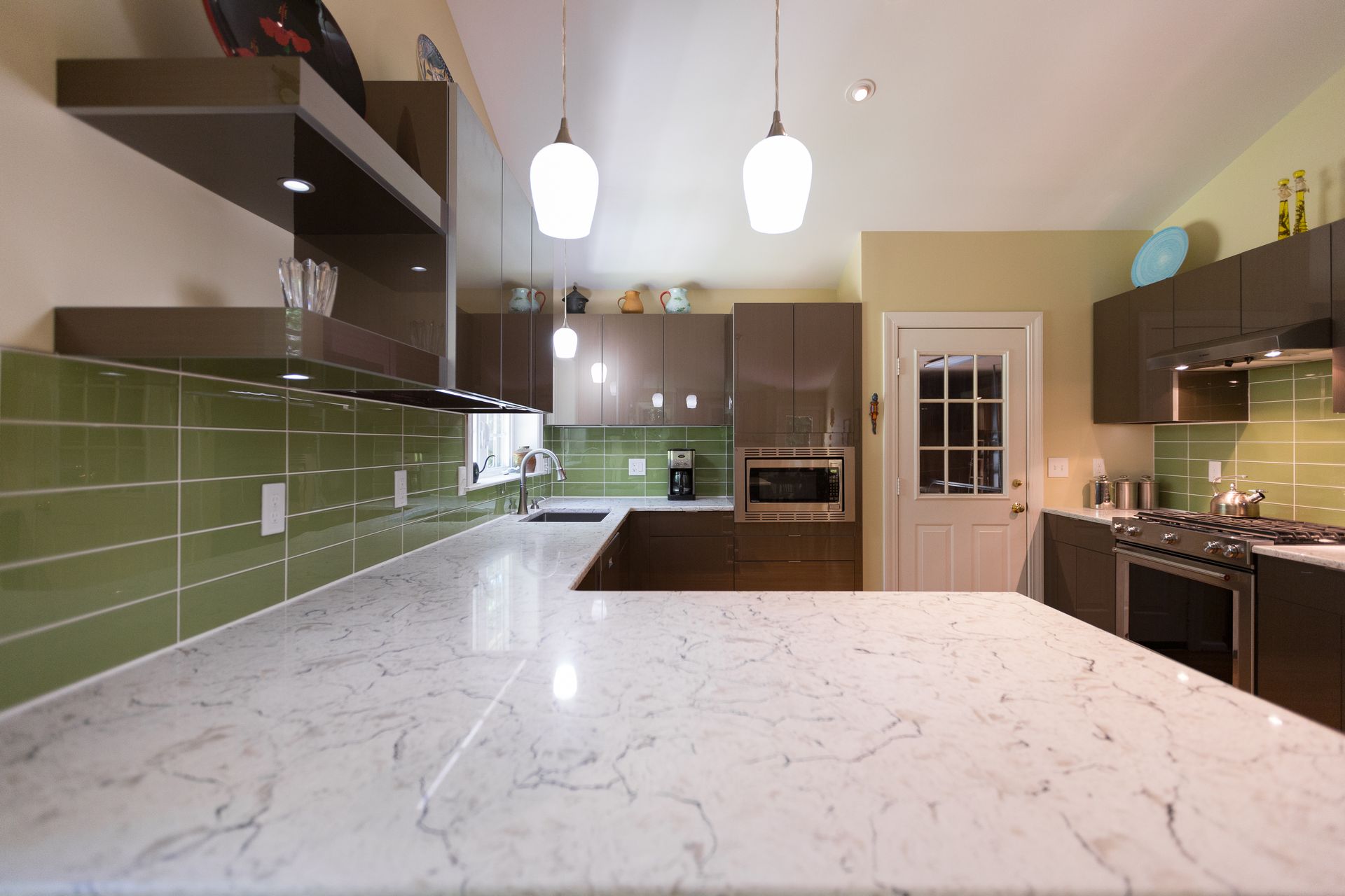 Modern kitchen with white marble island, green tile backsplash, dark wood cabinets, and pendant lights