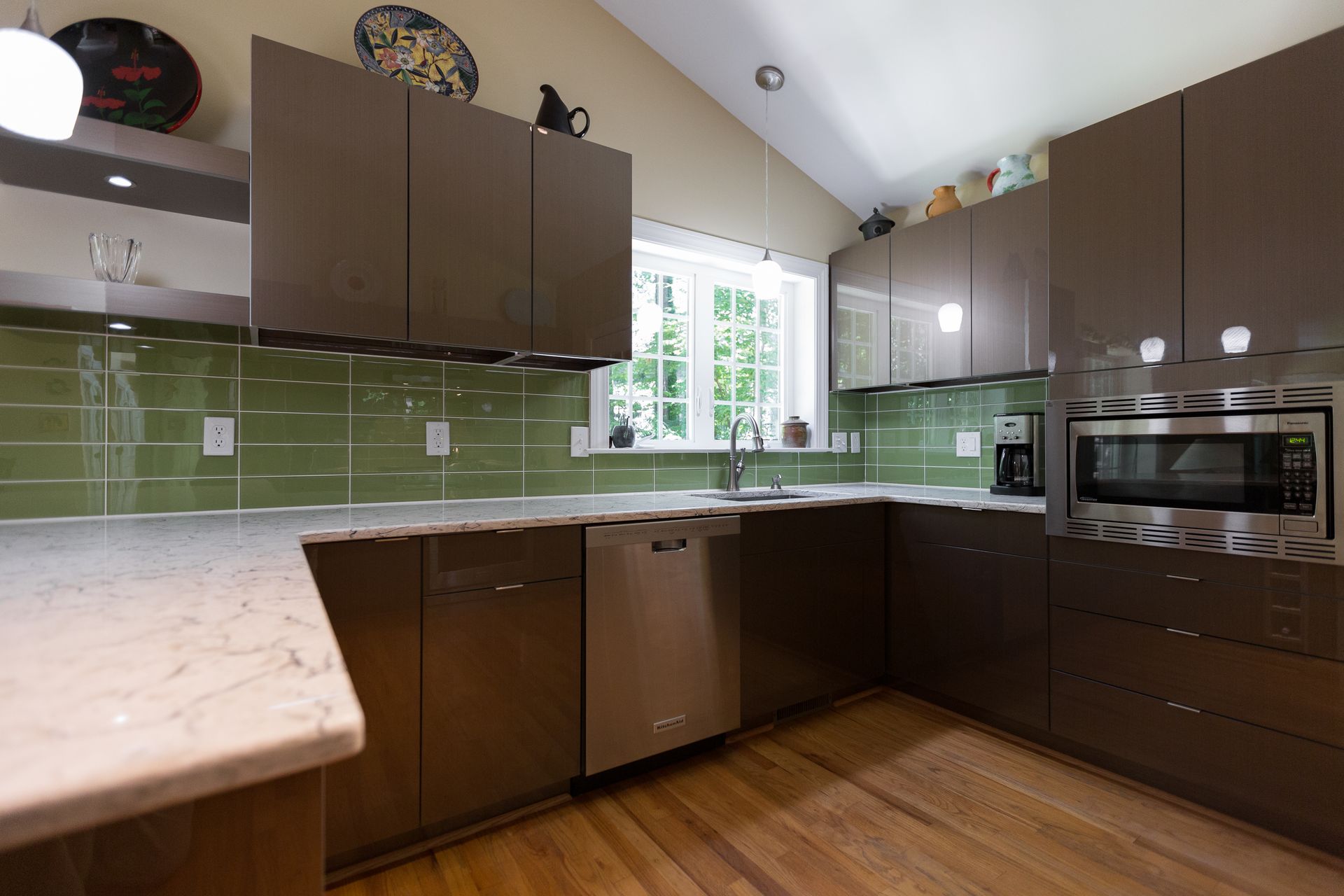 Modern kitchen with dark cabinets, green tile backsplash, stainless appliances, and a large window