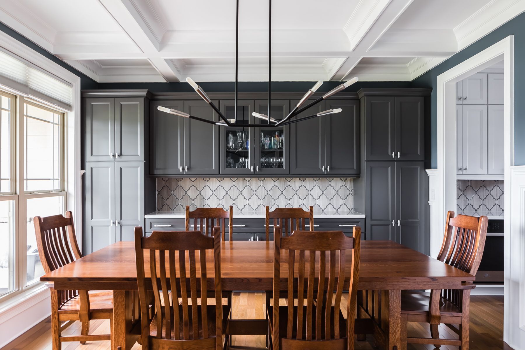 Elegant dining room with dark cabinets, wooden table, and chairs under a coffered ceiling.