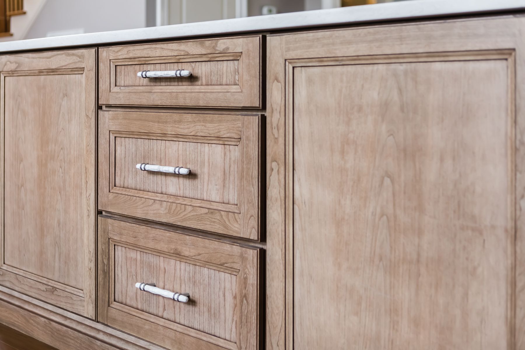Light wood kitchen cabinets with three drawers and silver handles beside a cabinet door