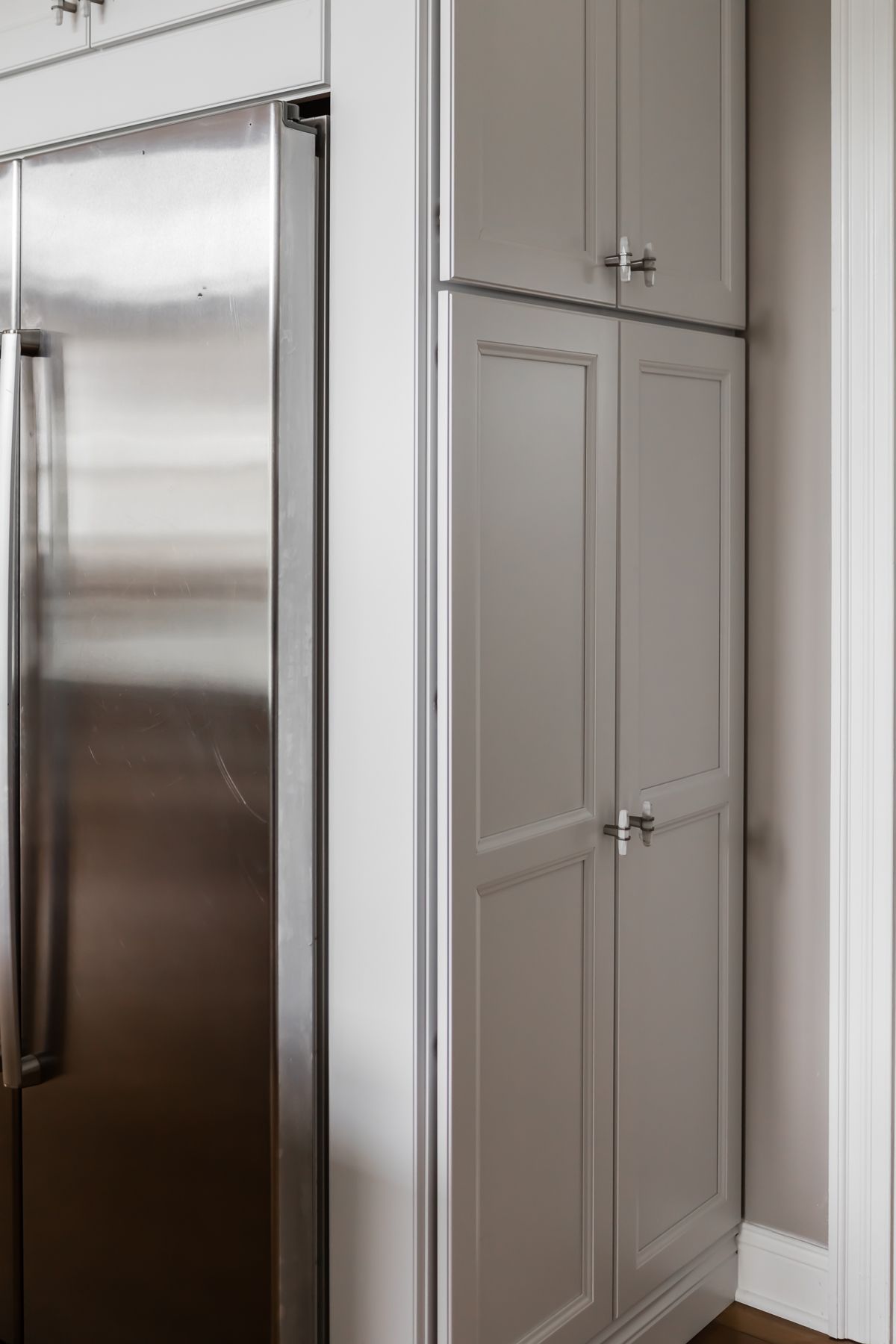 Tall gray pantry cabinets beside a stainless steel refrigerator in a modern kitchen