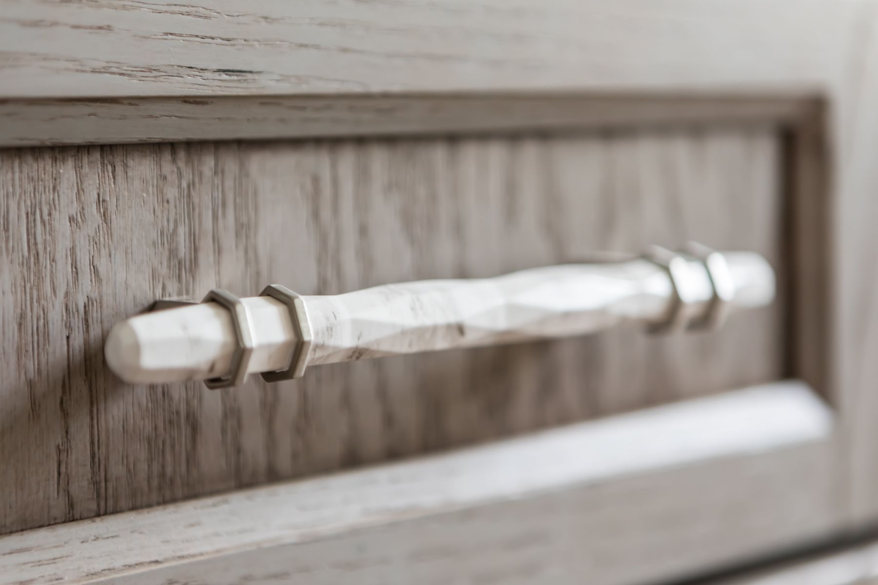 Close-up of a silver cabinet drawer pull on a light wood panel