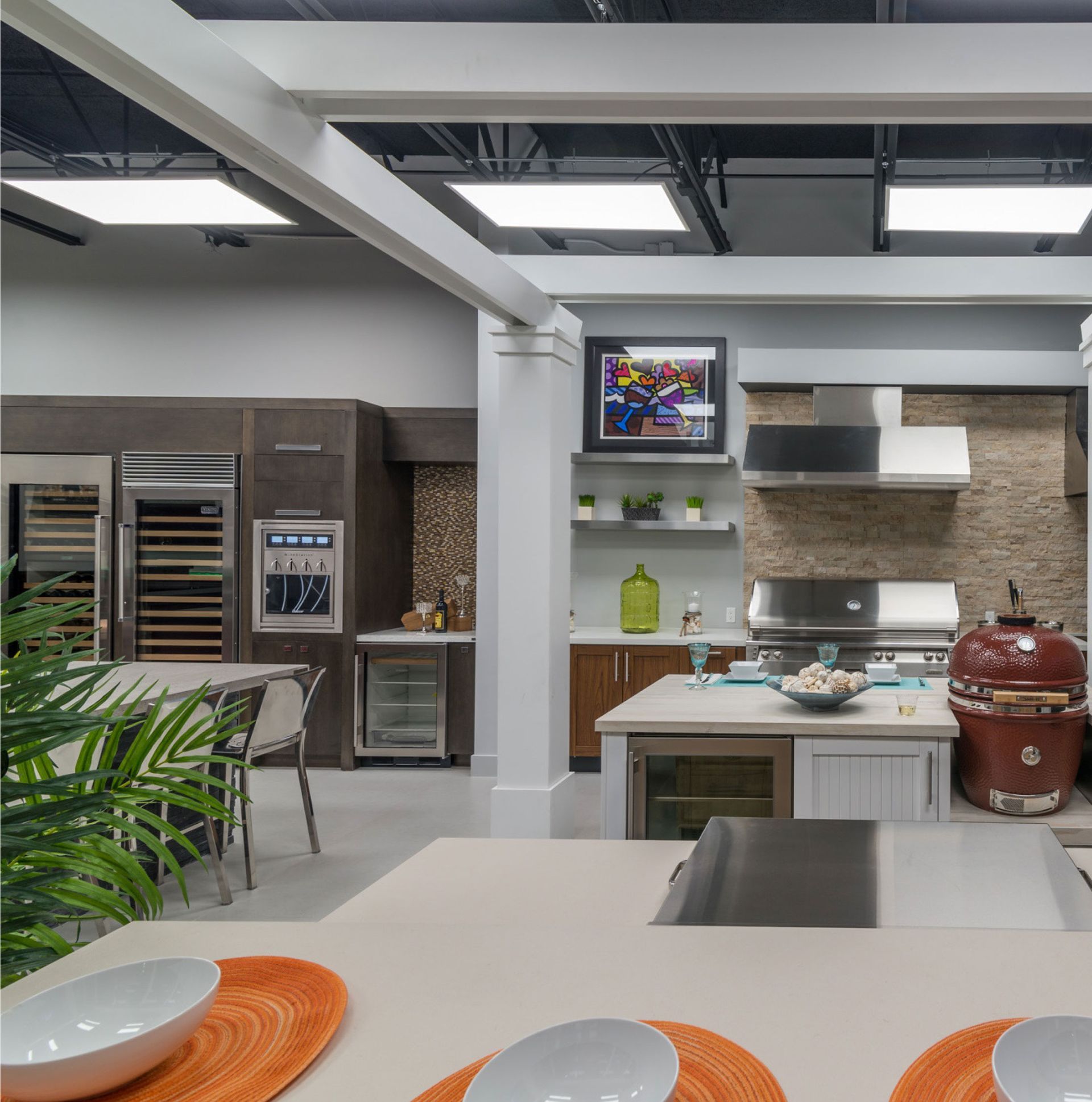 Modern open kitchen with gray cabinets, white island, red ceramic grill, and dining table in foreground