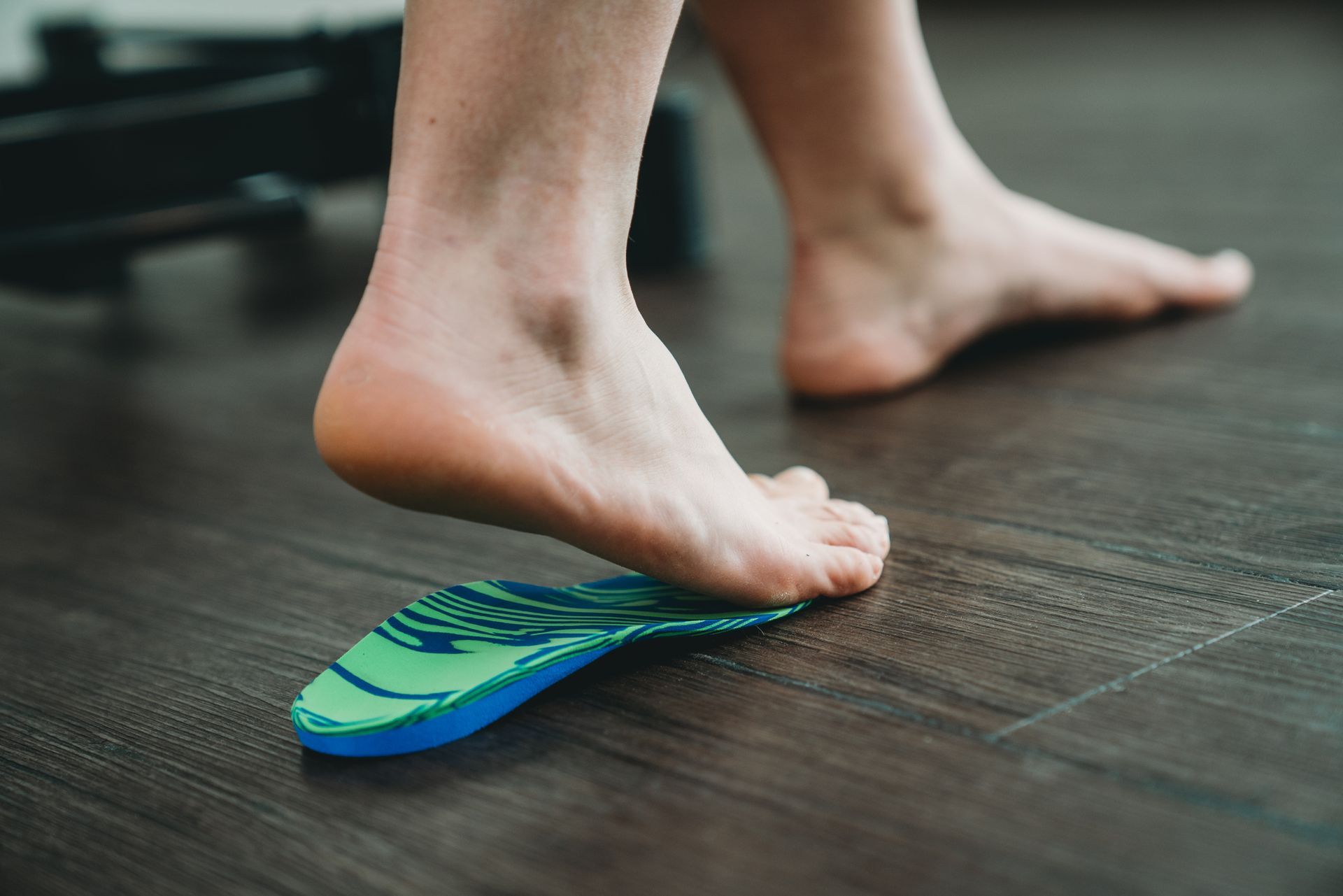 A person 's foot is standing on a green and blue insole on a wooden floor.