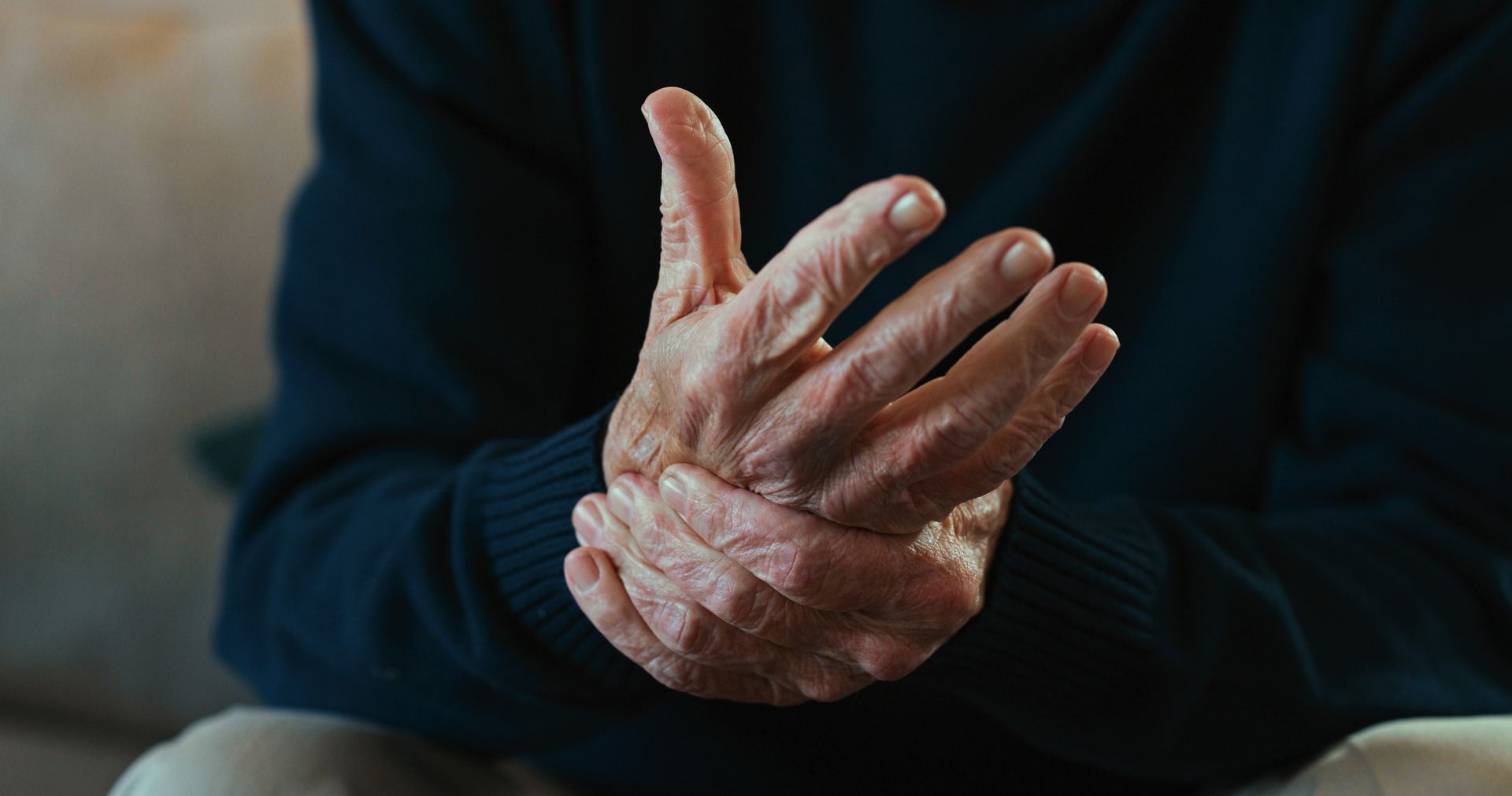 An elderly man is holding his wrist in pain.