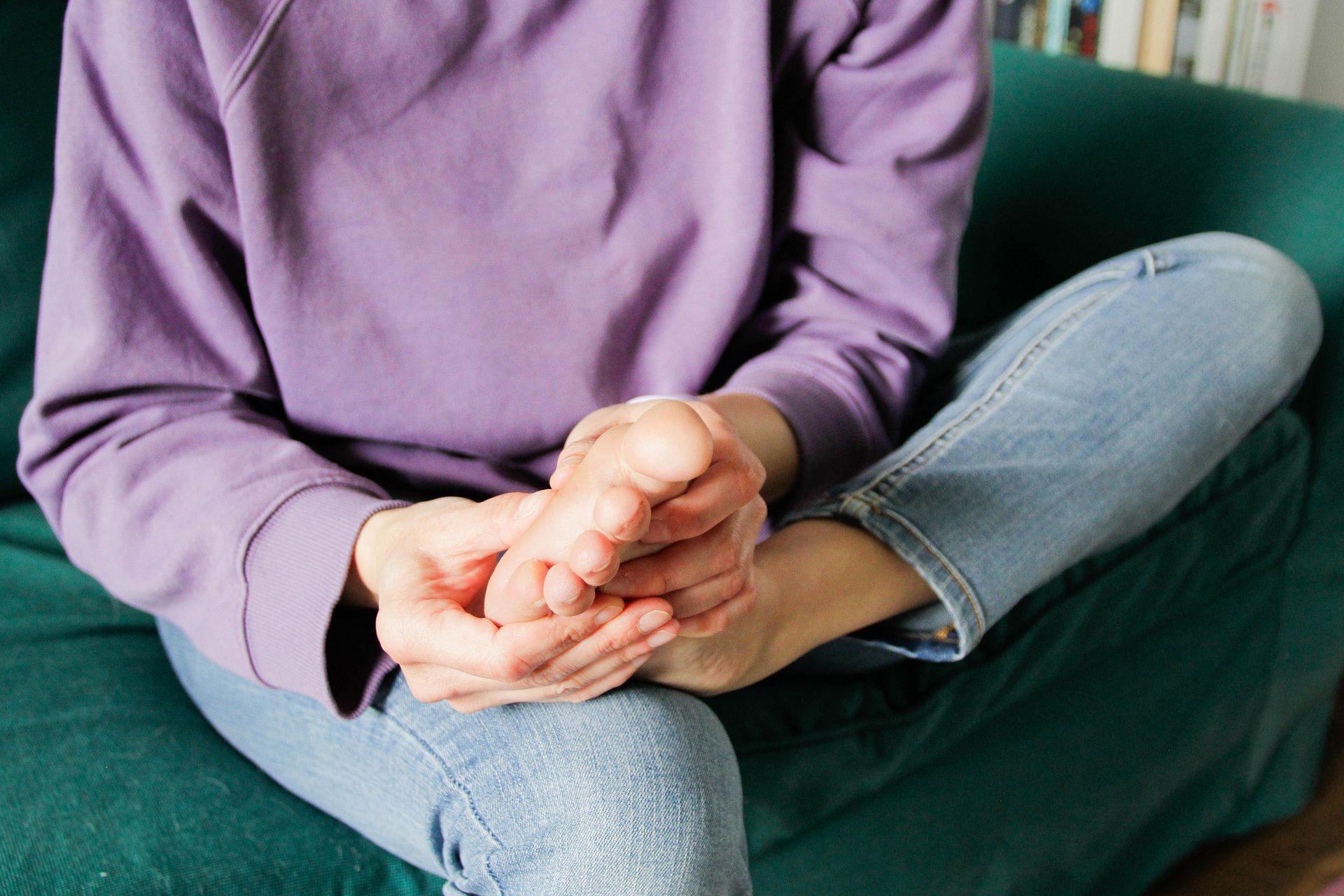 A person is sitting on a couch with their legs crossed and holding their feet.