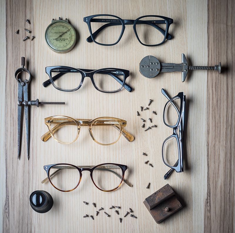 Eyeglasses and tools, including a compass and calipers, arranged on a wood surface, showcasing eyewear.