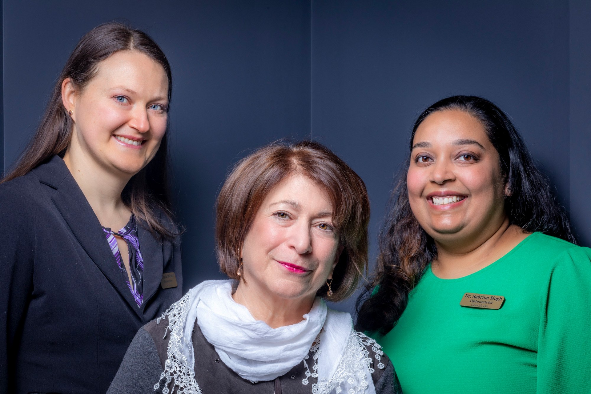 Three women smiling in front of a dark blue background.