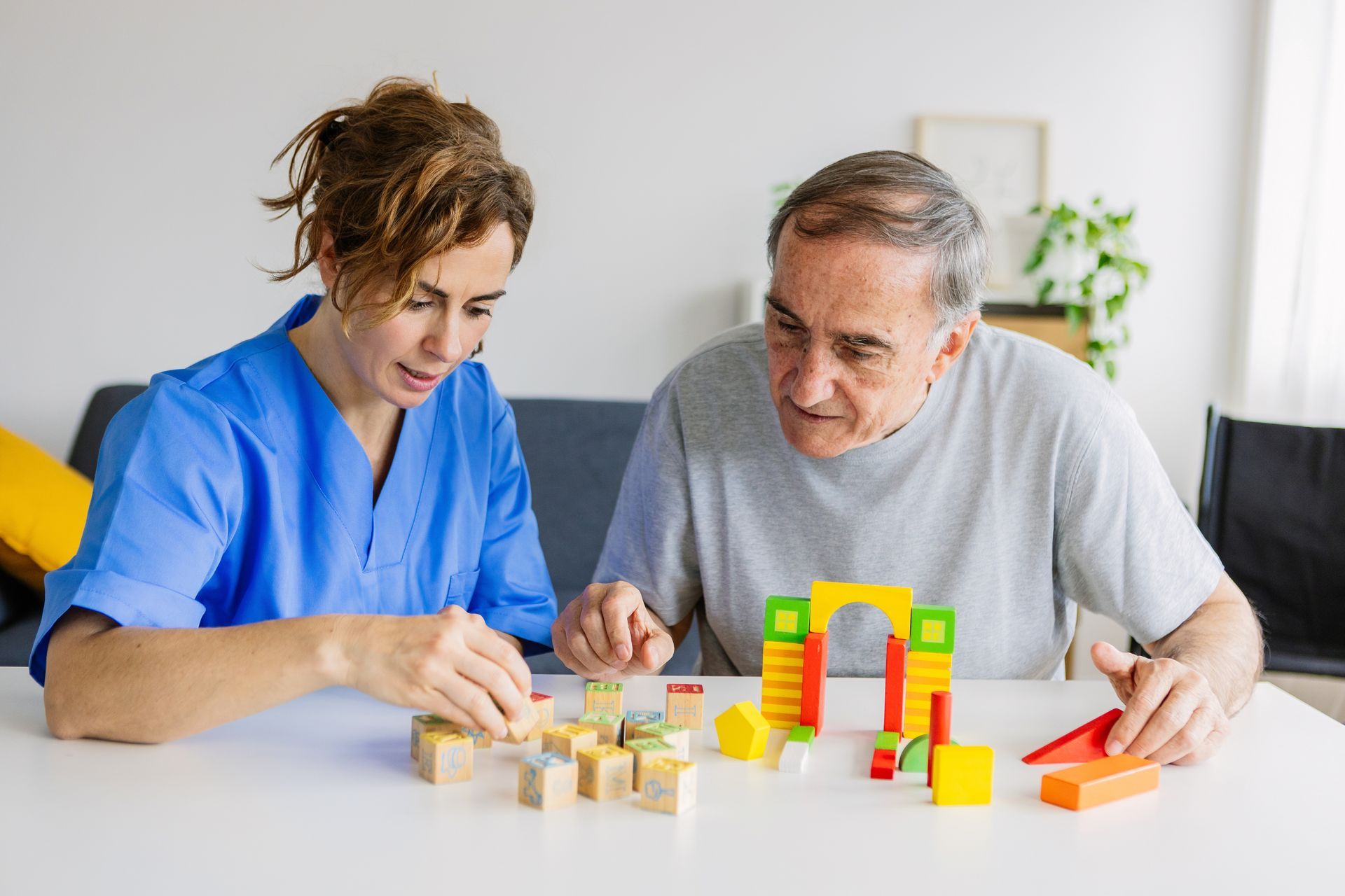 A female caregiver is helping a senior man with wooden shape puzzles for dementia support. A female caregiver is helping a senior man with wooden shape puzzles for dementia support.