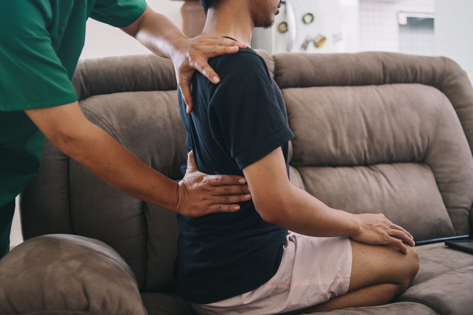 A person receiving a back adjustment on a couch. Chiropractor in green shirt, patient in black tee. A person receiving a back adjustment on a couch. Chiropractor in green shirt, patient in black tee.