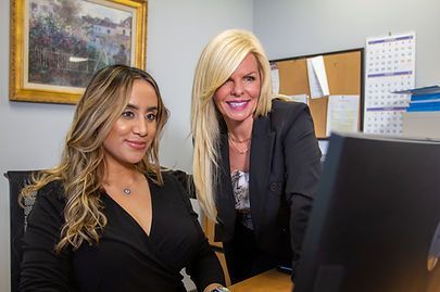 Two women in office setting, looking at computer. One blond, one brunette, both smiling. Two women in office setting, looking at computer. One blond, one brunette, both smiling.
