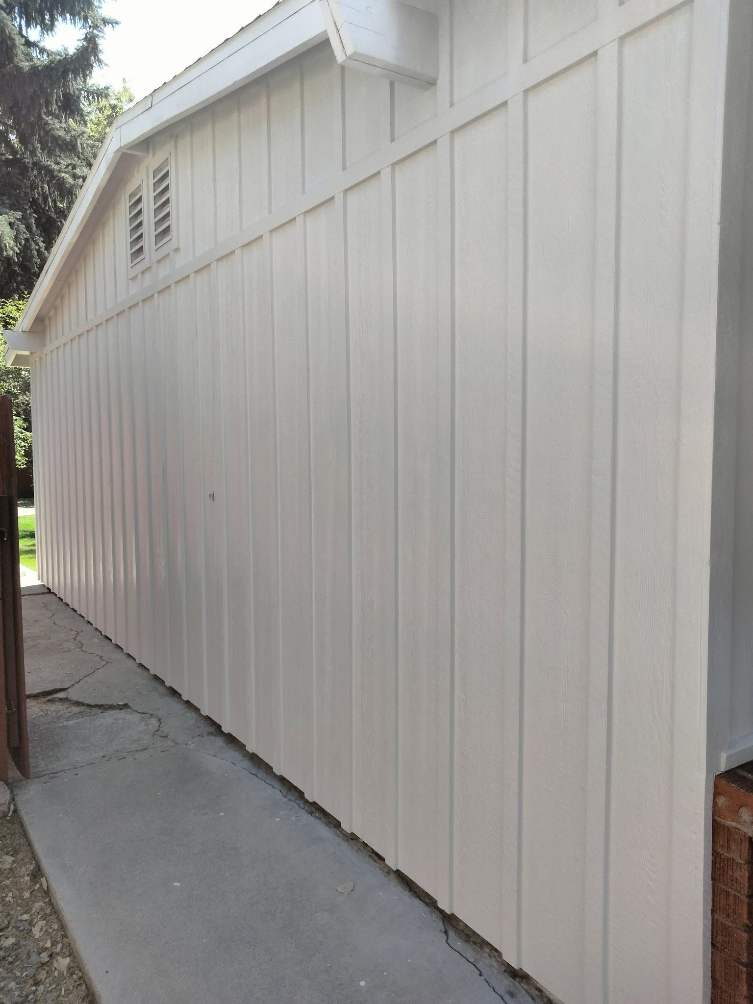 White wooden shed wall along a narrow concrete walkway outdoors.