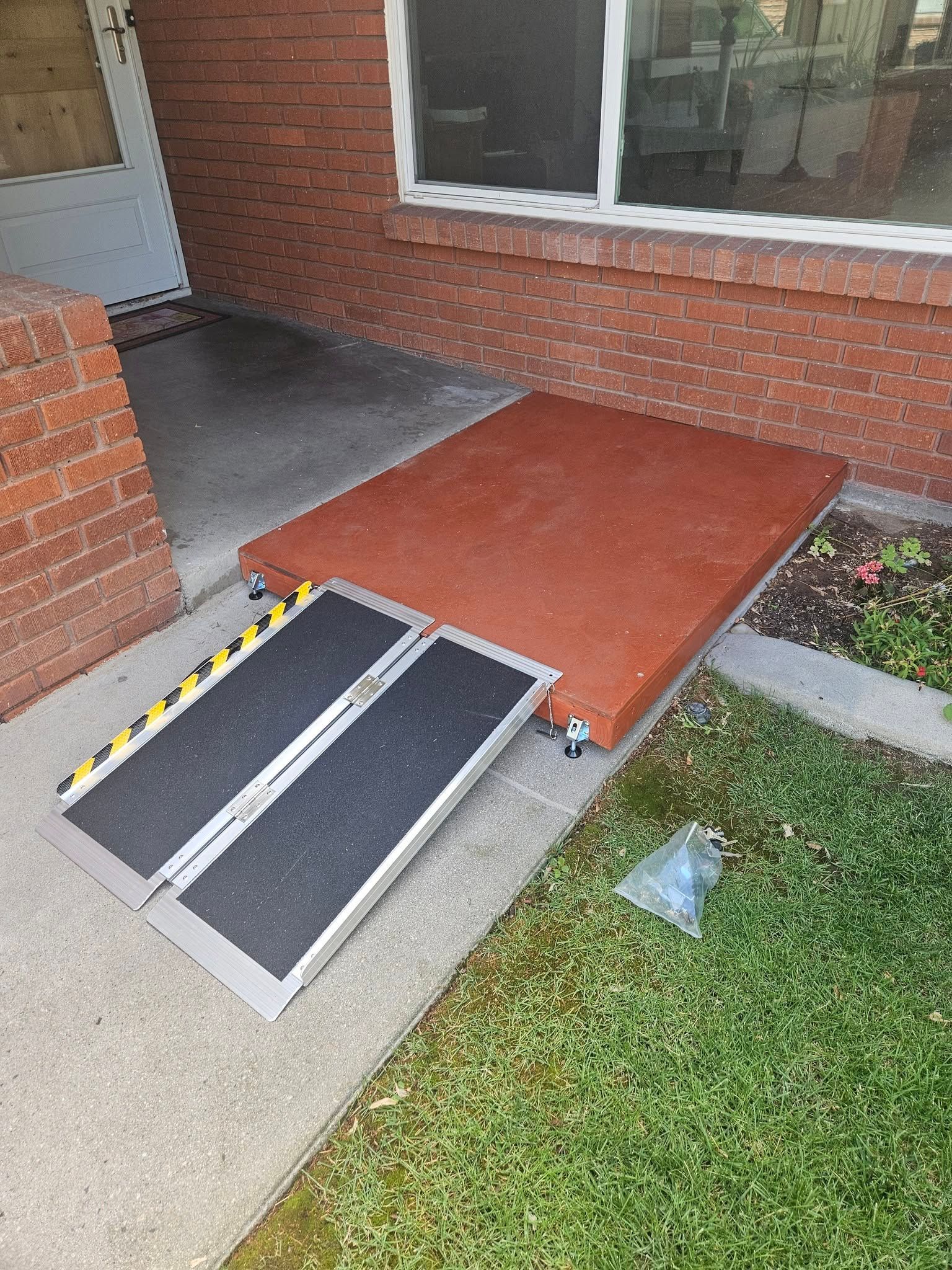 Portable ramps at a brick house entrance with a small step and grass nearby