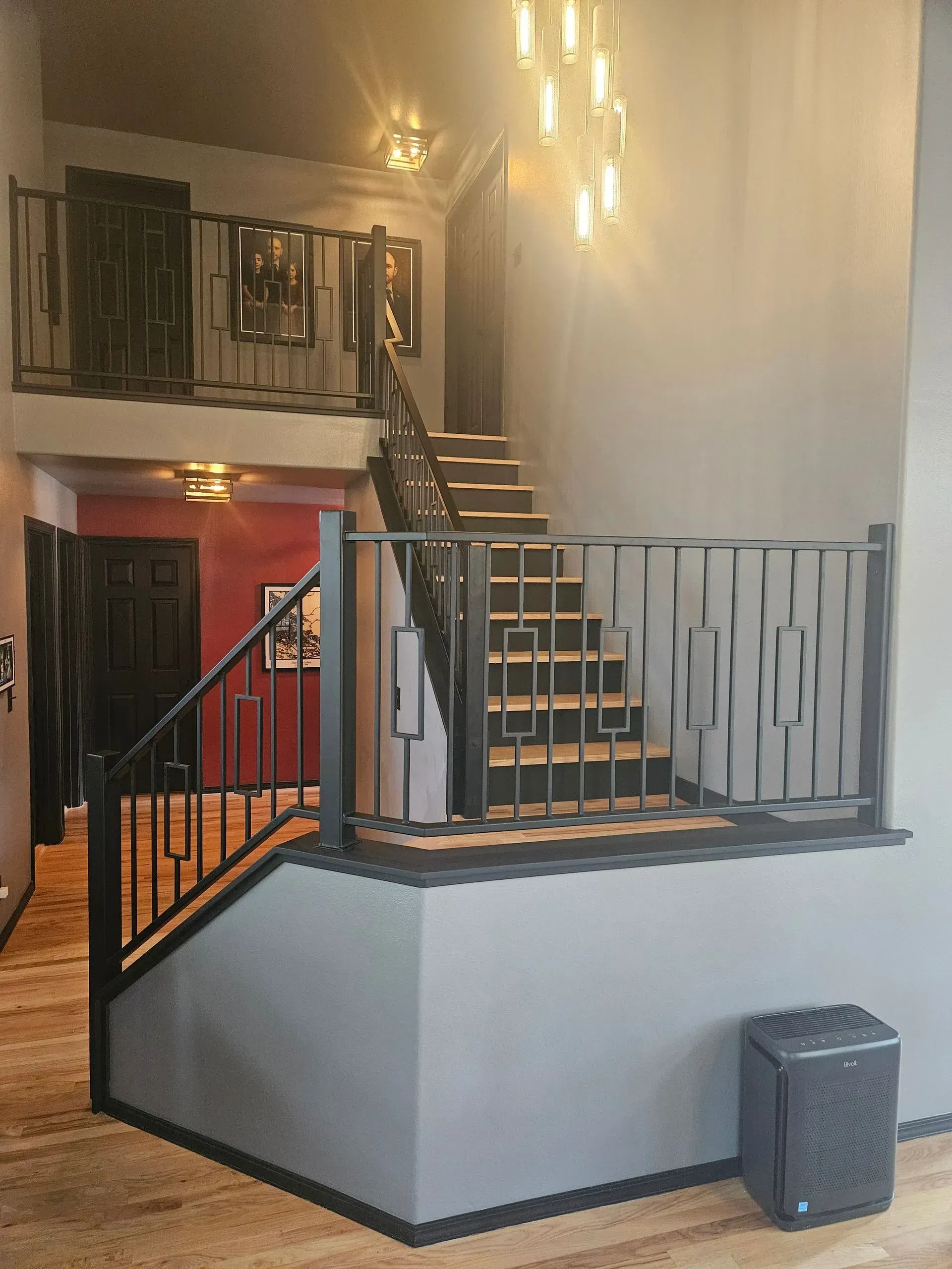Indoor stairway with black railings, white walls, and a red door in a two-story lobby