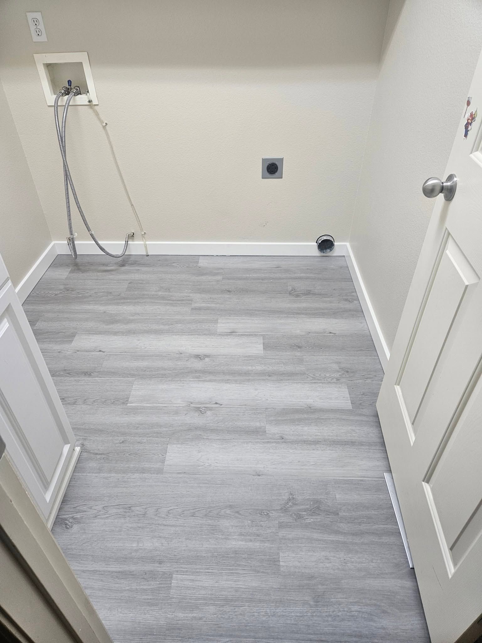 Empty laundry room with gray wood-look floor, white walls, sink hookups, and a radiator on the right.