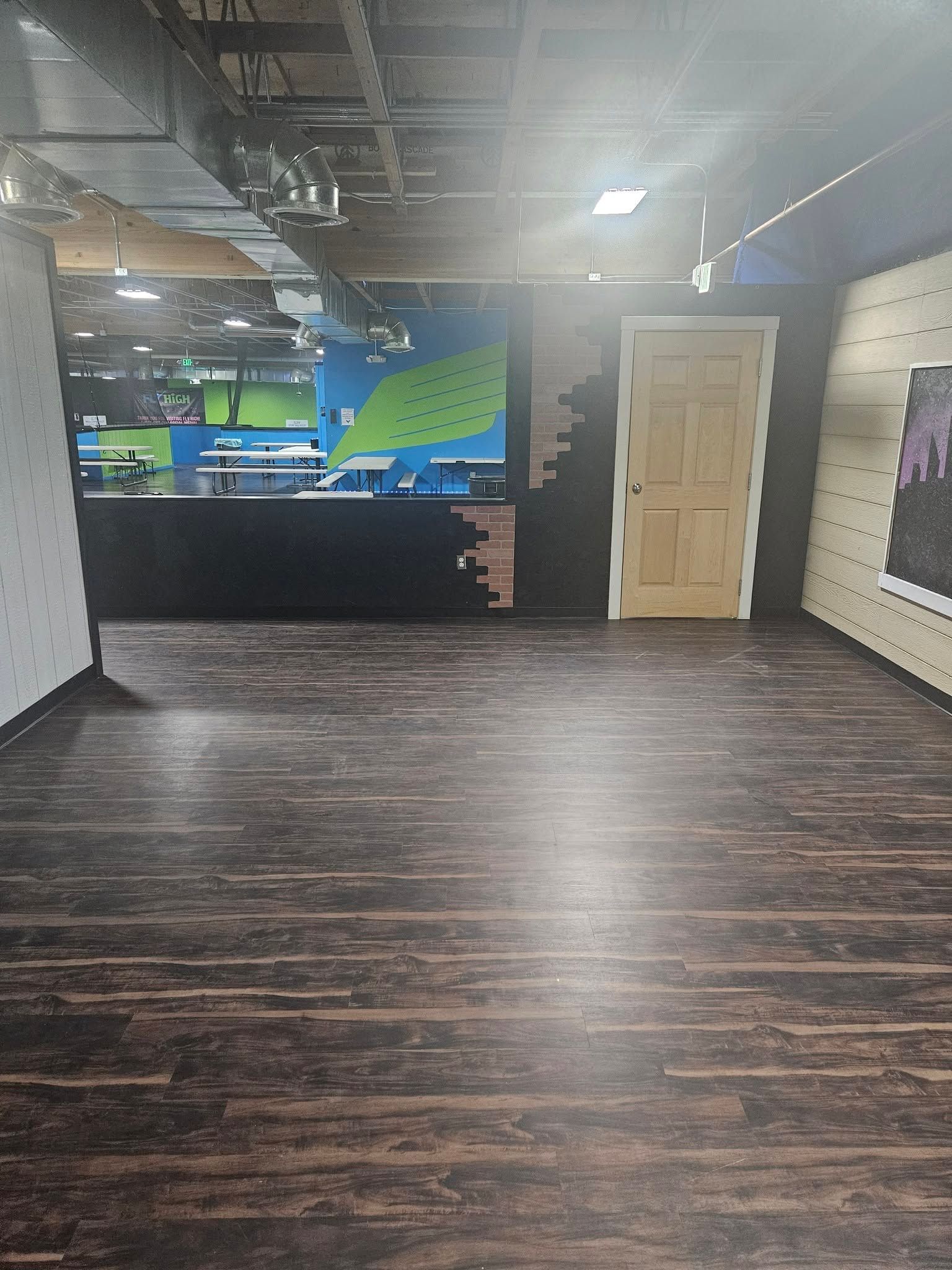 Empty lobby with dark wood floor, black front desk, beige door, and exposed ceiling lights.