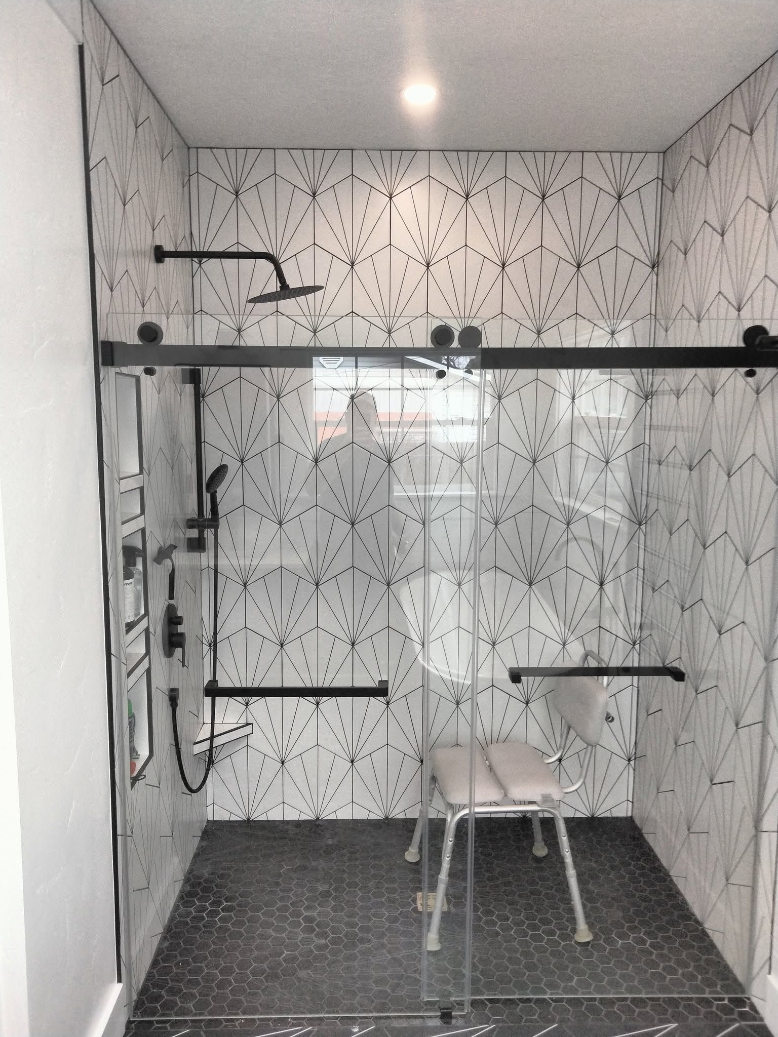 Small tiled shower room with bench, grab bars, and handheld showerhead