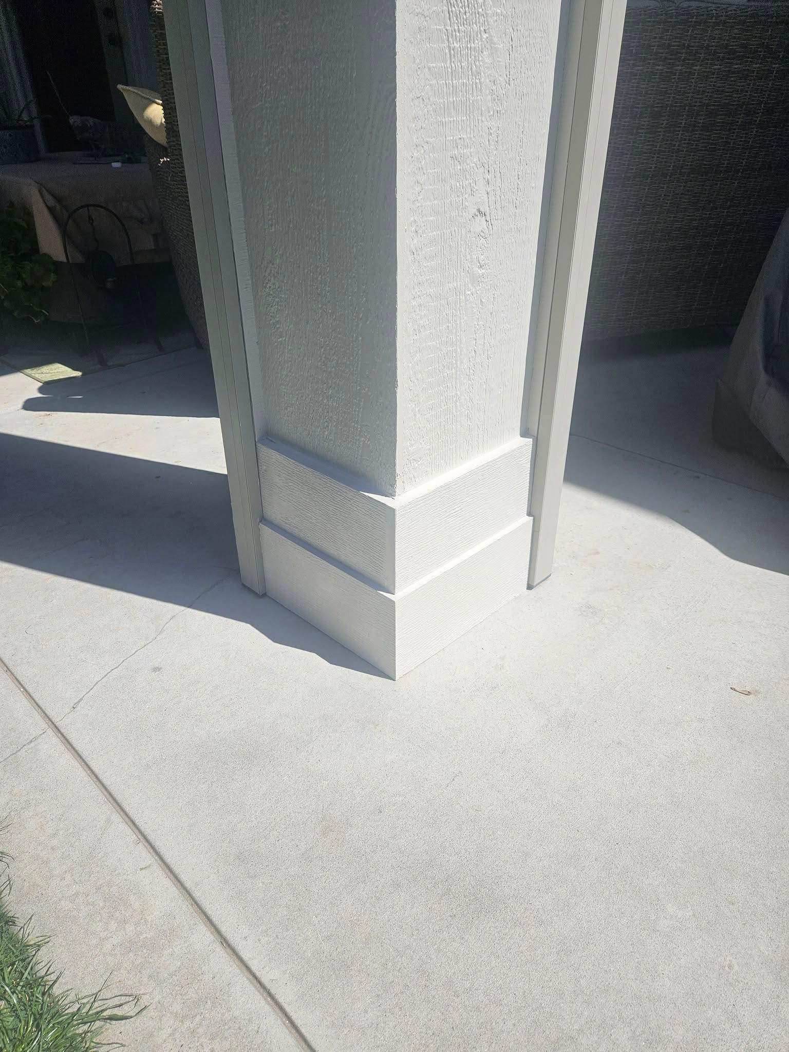 Concrete pillar on a sidewalk next to a building entrance, lit by sunlight and shadow.