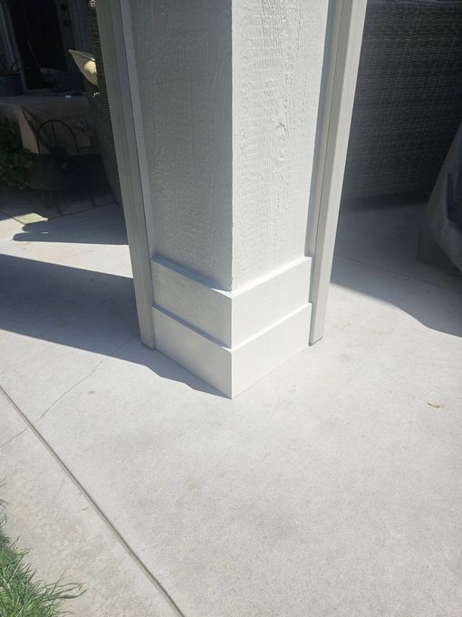 Concrete pillar on a sidewalk next to a building entrance, lit by sunlight and shadow.