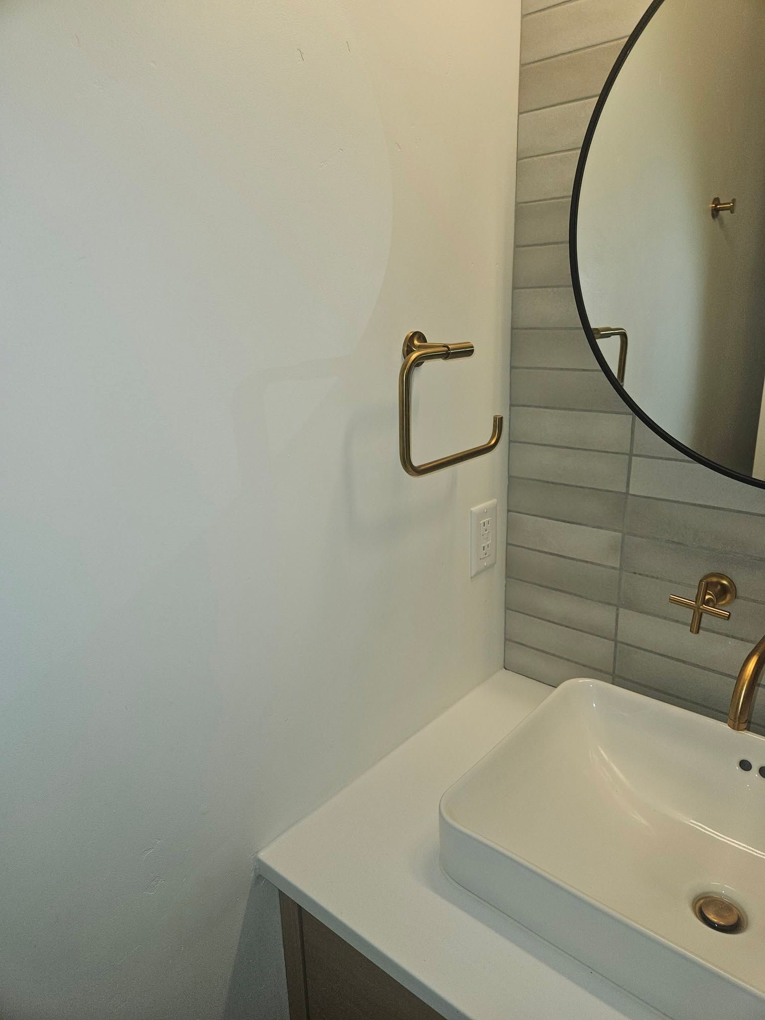 Small bathroom sink with round mirror, gold faucet, and wall-mounted grab bar beside a tiled shower.