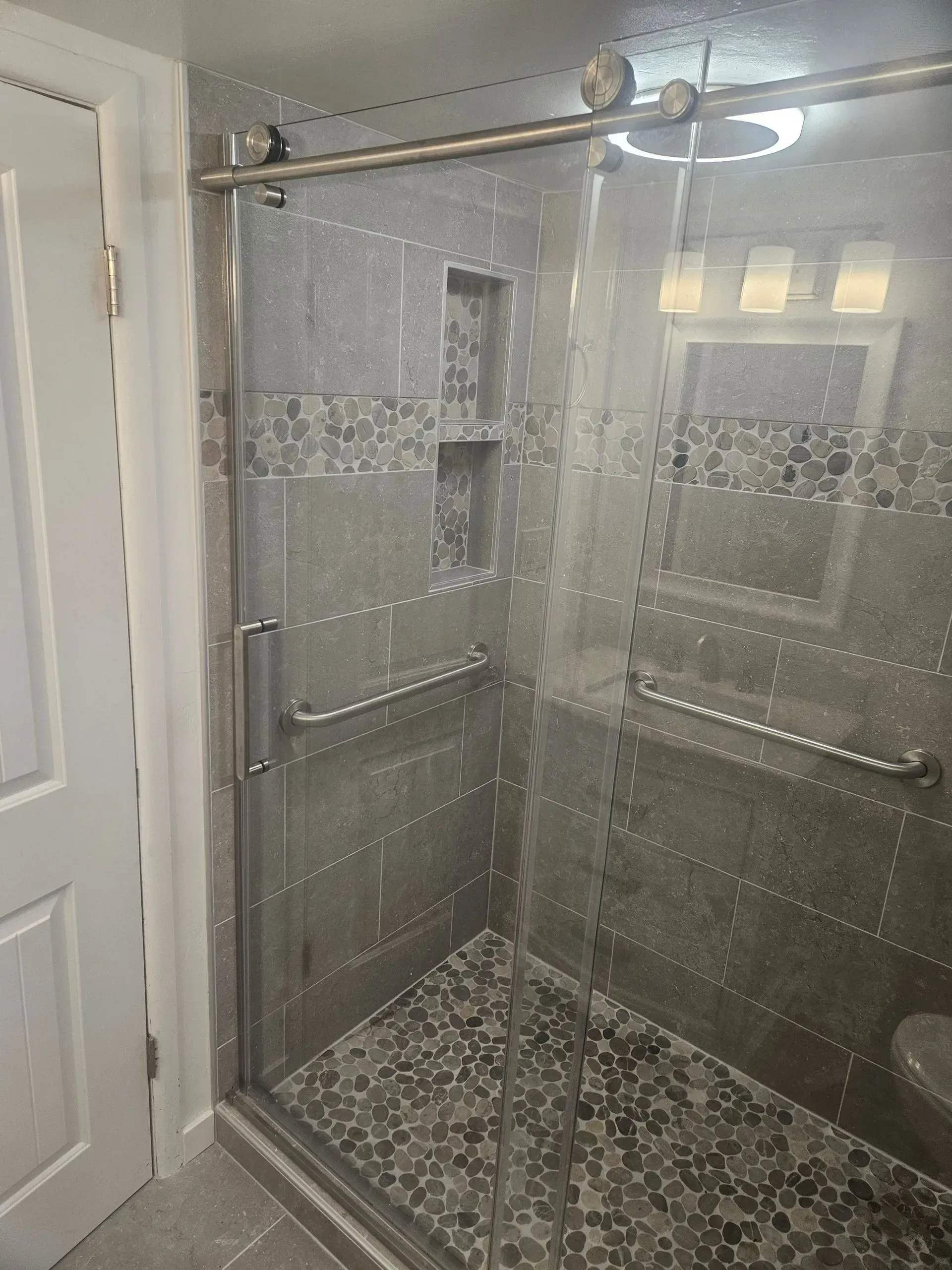 Glass shower enclosure with chrome bars and pebble-style tile floor in a bathroom
