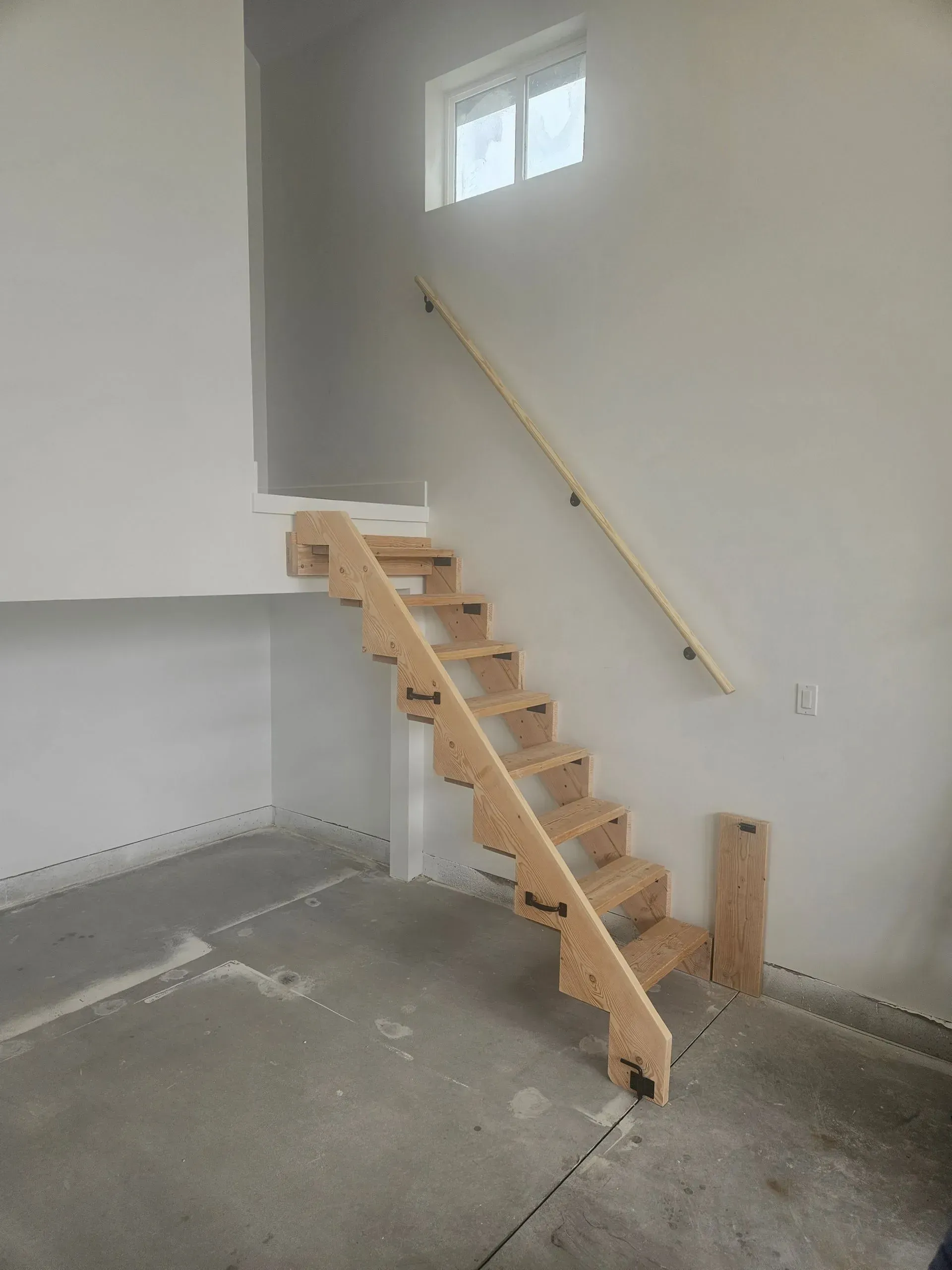 Unfinished indoor staircase with wooden steps and handrail in a white garage or basement room