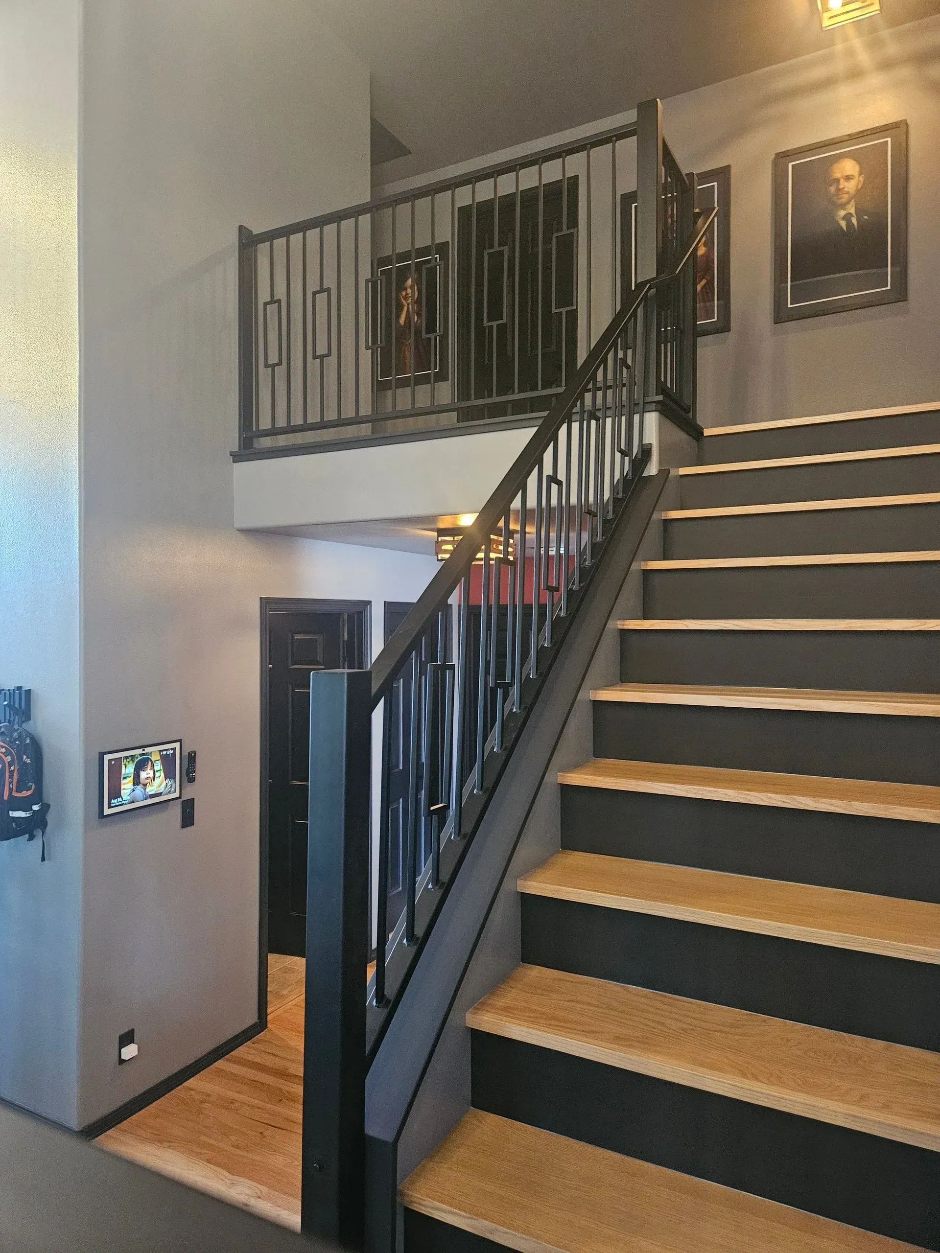 Interior staircase with black railing, tan carpeted steps, and a lofted landing in a hallway.