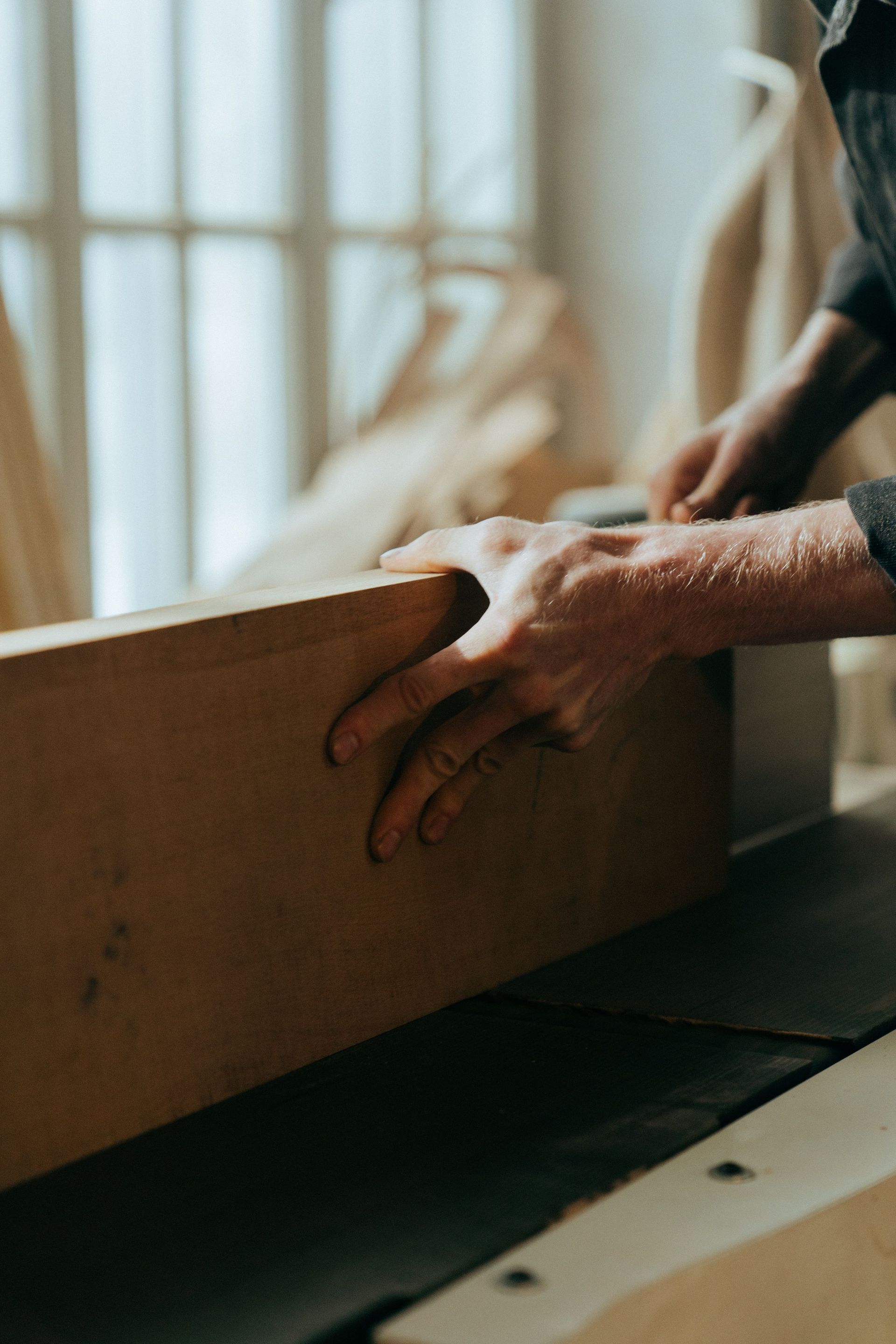 Hands moving a cardboard box on a worktable by a window