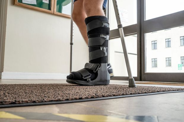 Persona con tutore alla gamba e stampelle in piedi su un tappeto vicino a una finestra.