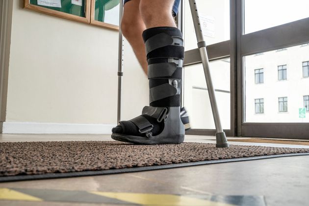 Persona con tutore alla gamba e stampelle in piedi su un tappeto vicino a una finestra.