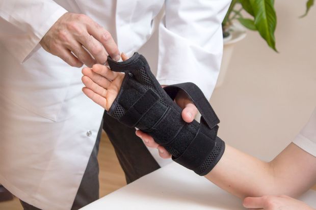 Operatore sanitario che applica un tutore nero al polso di un paziente.