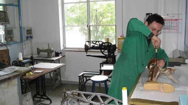 Una persona con una camicia verde lavora l'argilla al tornio in un luminoso studio di ceramica.