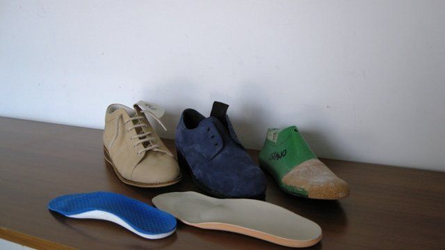 Diverse paia di scarpe e solette rimovibili sono esposte su un tavolo appoggiato a una parete spoglia.