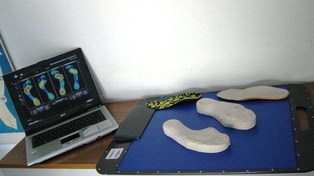 Un computer portatile mostra le scansioni dei piedi accanto a delle solette personalizzate su un banco da lavoro blu.