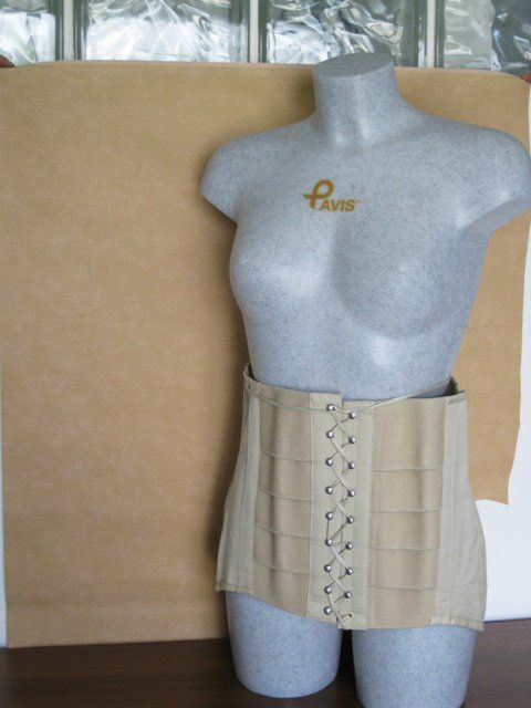 Manichino grigio che indossa un corsetto beige con lacci in vita, su uno sfondo color cuoio.