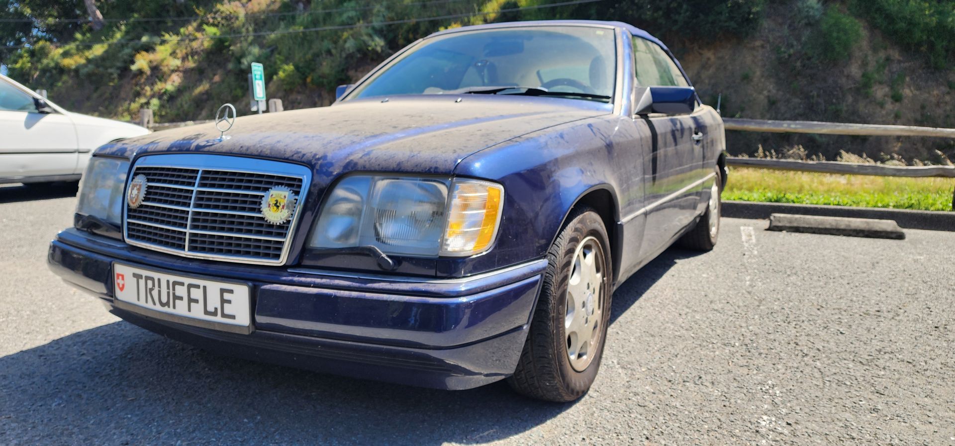 Blue sedan parked by a road in bright sunlight, front-left view