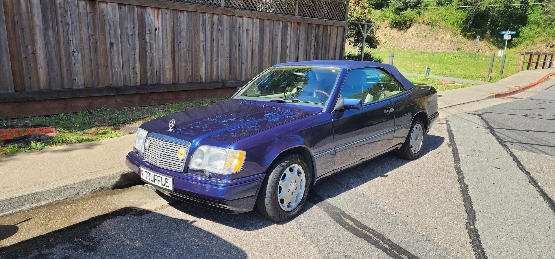 Purple sports coupe parked on a sunny street beside a wooden fence