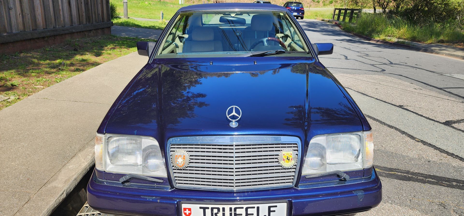 Blue Mercedes sedan parked on a street, front view in sunlight