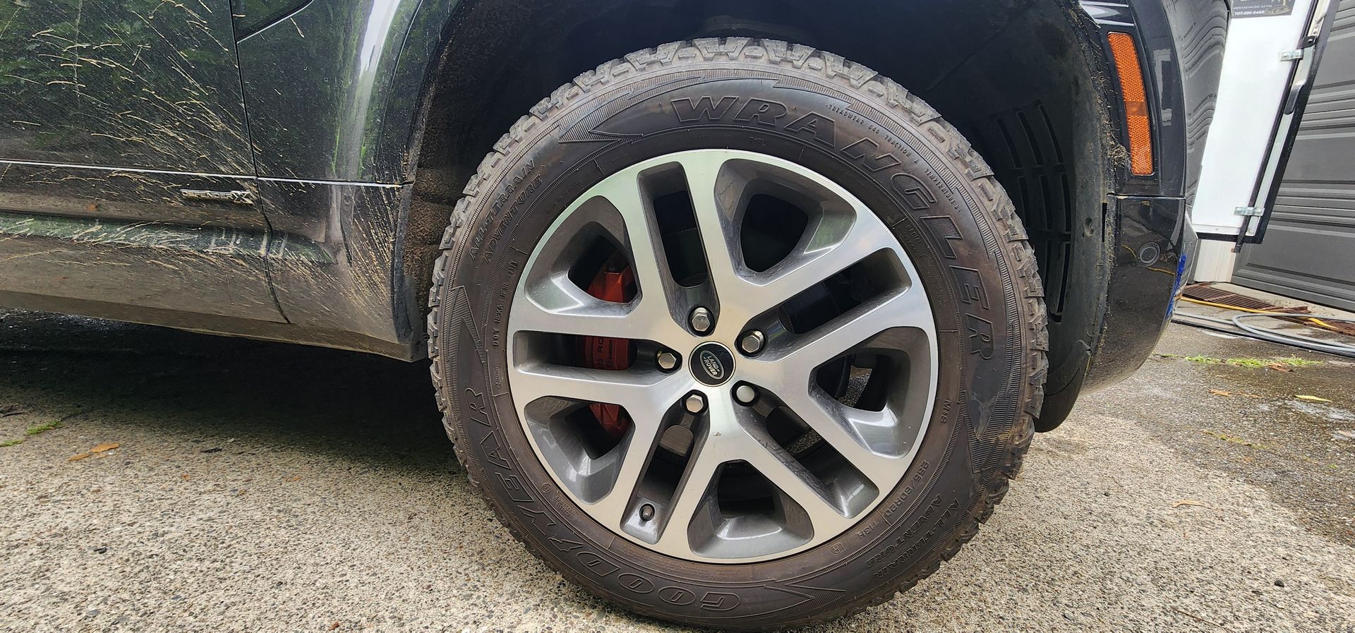 Close-up of a black SUV’s front wheel and tire on a wet gravel surface.