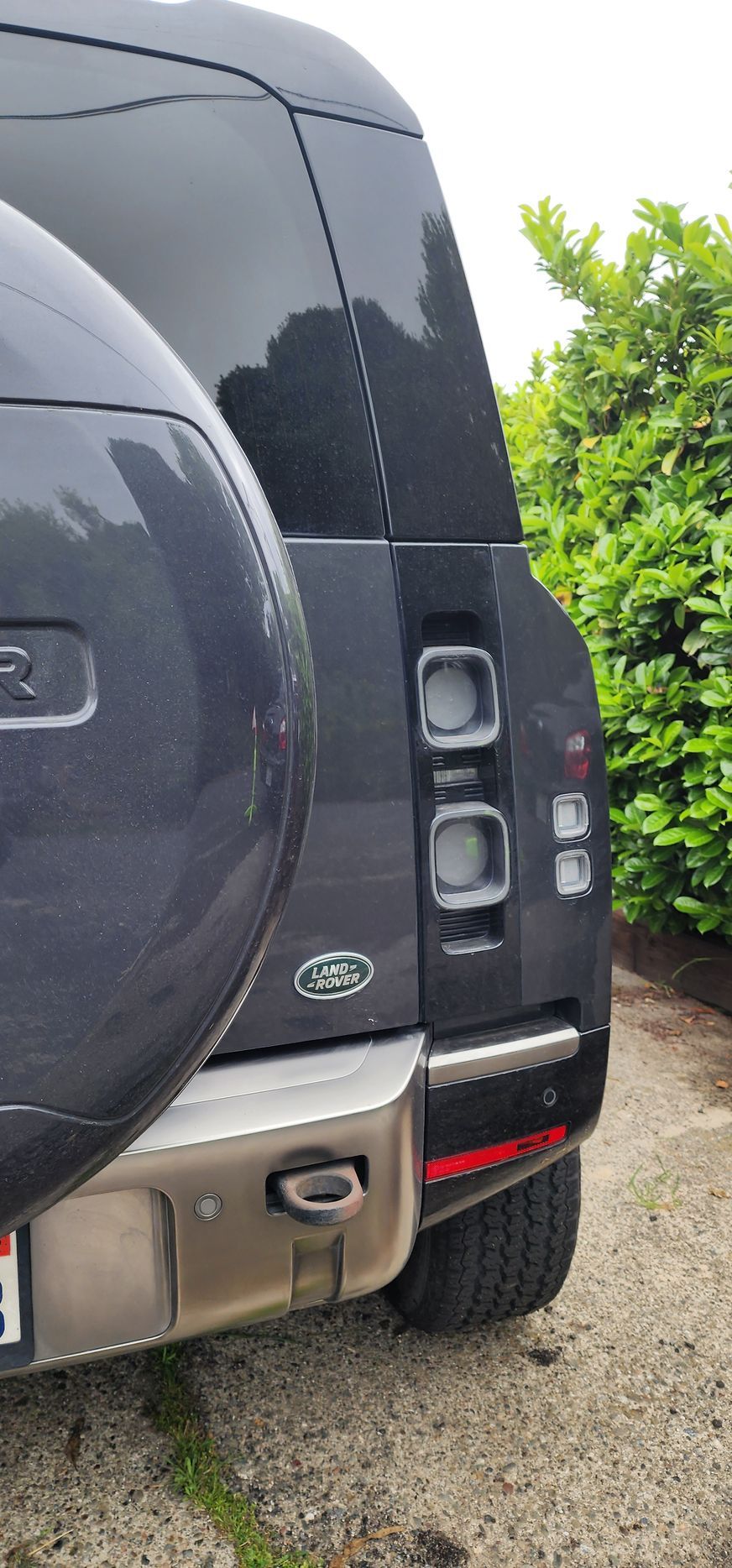 Rear view of a dark SUV parked on gravel, showing the tail light and spare tire cover.