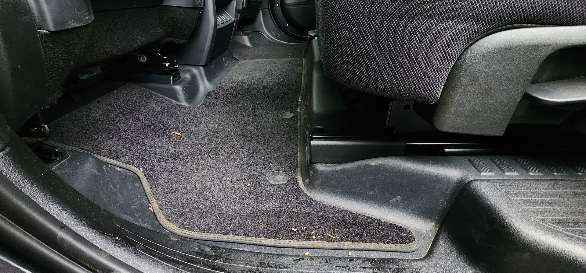 Close-up of a car’s black carpeted floor and center tunnel area with textured plastic trim.