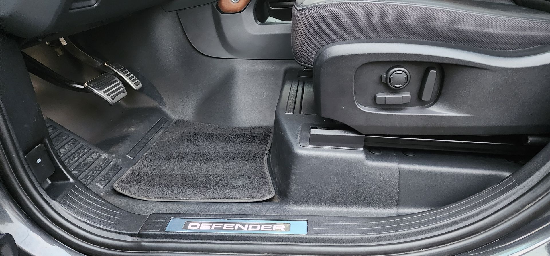 Car door sill and footwell with black floor mat and seat adjustment control visible