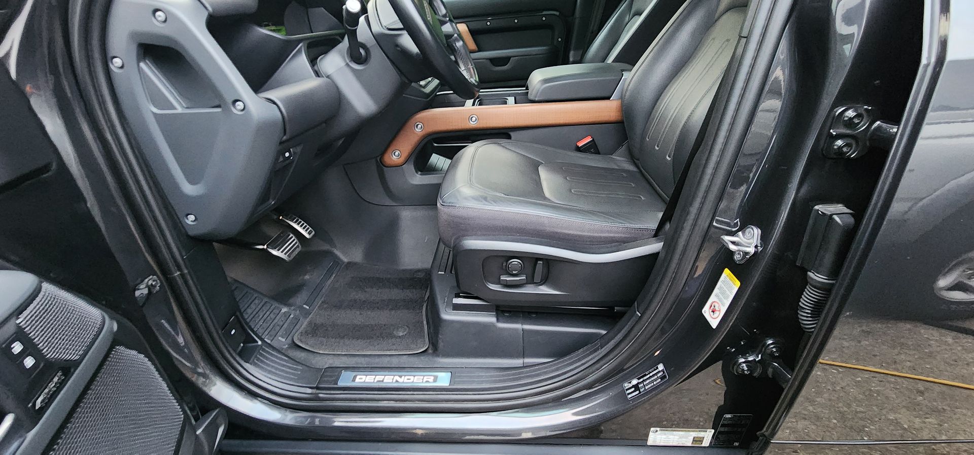 Open car door showing gray front seat, wood trim, and illuminated running board.