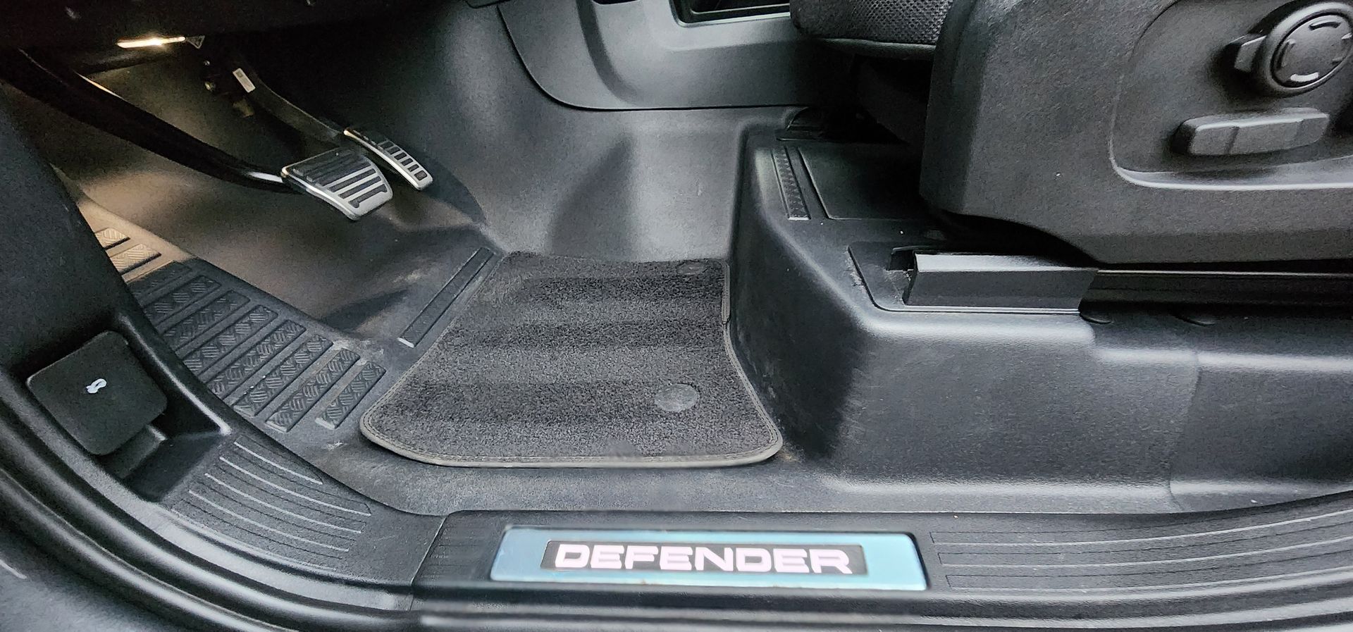Car footwell with black floor mats and a Defender-branded door sill trim