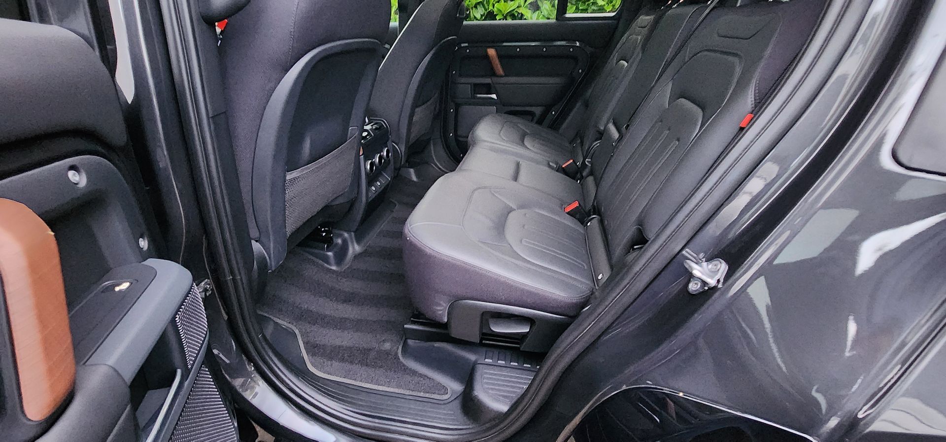 Rear seats of a car with gray upholstery and black floor mats, viewed from the open door