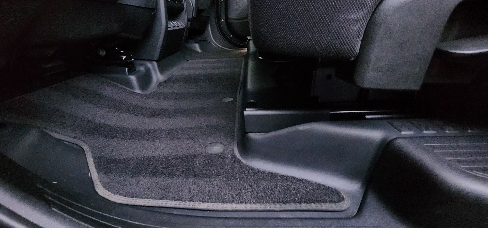 Close-up of a car’s rear floor and center console area with black carpet and gray trim
