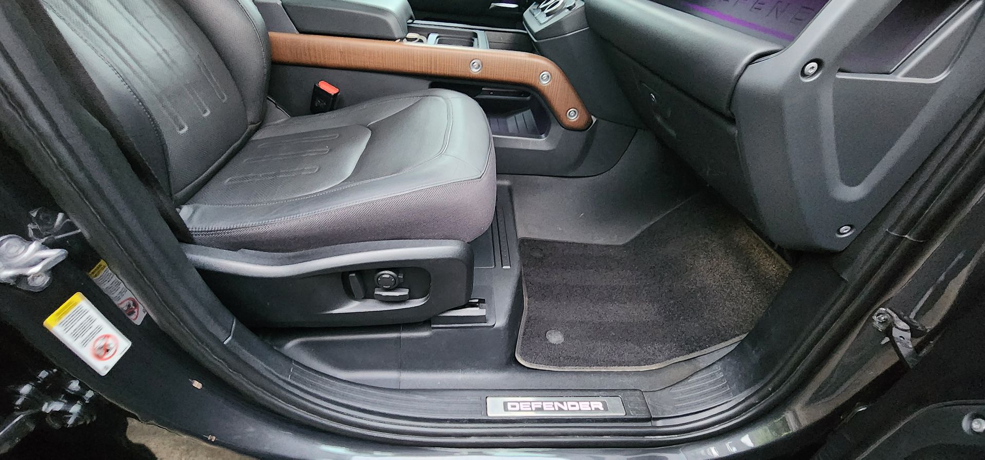Car interior with black leather seats, wood trim, and open door showing the front passenger footwell